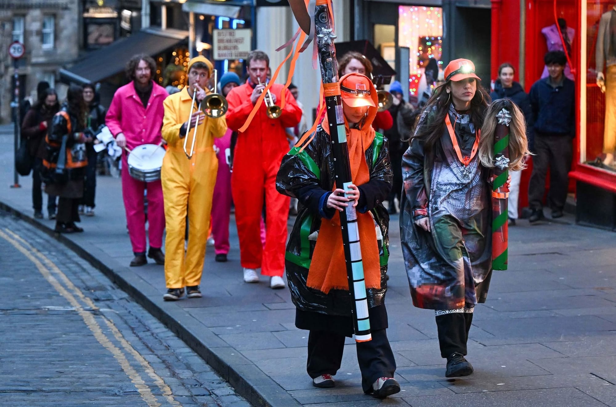 People wearing bright colours walking up a city street, some playing musical instruments. 