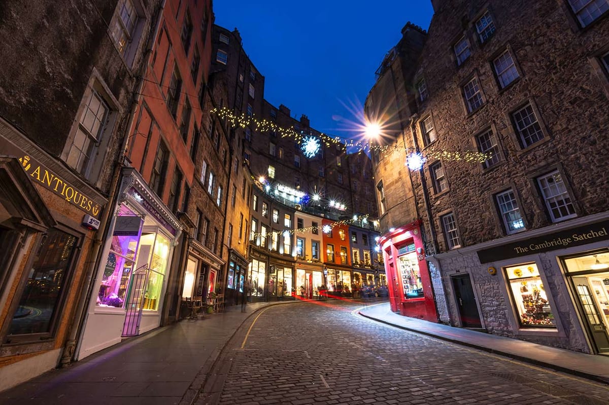 A cobbled hill flanked by shops and tall buildings either side, connected by festive lights above. 