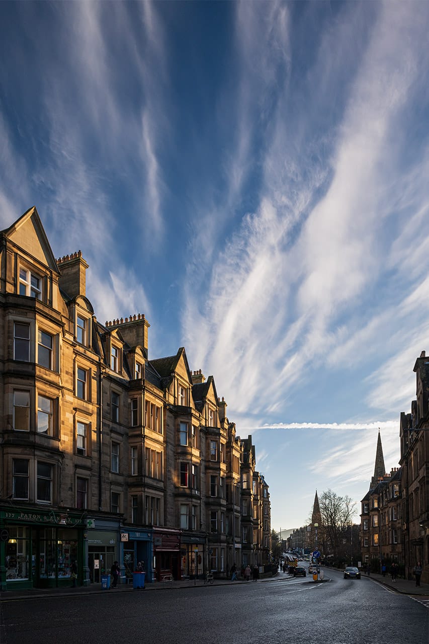 A city street with stripy cirrus clouds above. 
