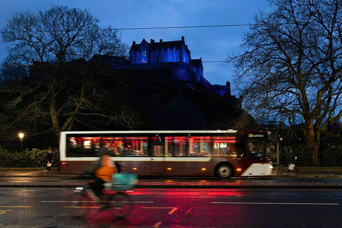 A person riding a bike going to the left and a bus going to the right on a street with a castle in the background. 
