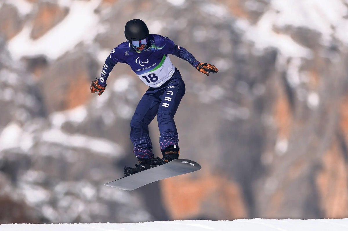 A snowboarder navigating a jump, with a mountain rockface in the background. 