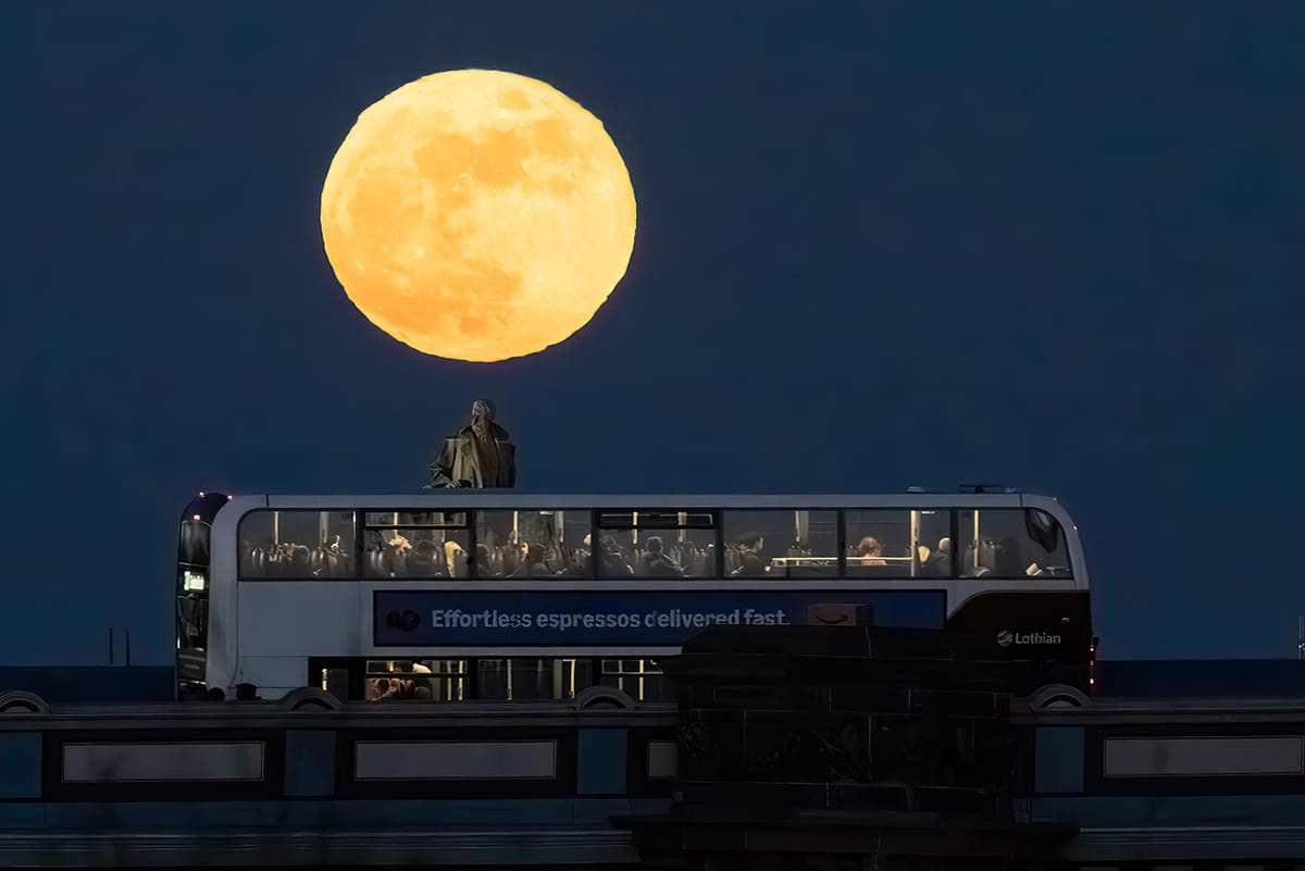 A bus on a city bridge with a full moon appearing in the sky behind. 