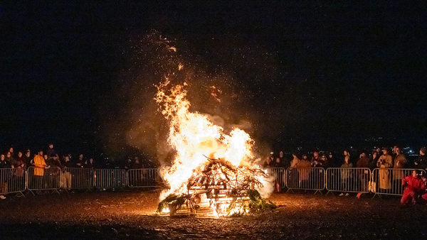 A crowd of people standing around a bonfire at night. 