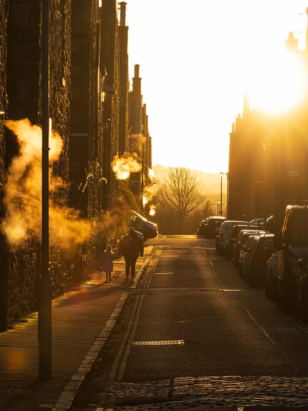 People walking in a residential street towards the sunset, with vapour from their breath visible in the light.