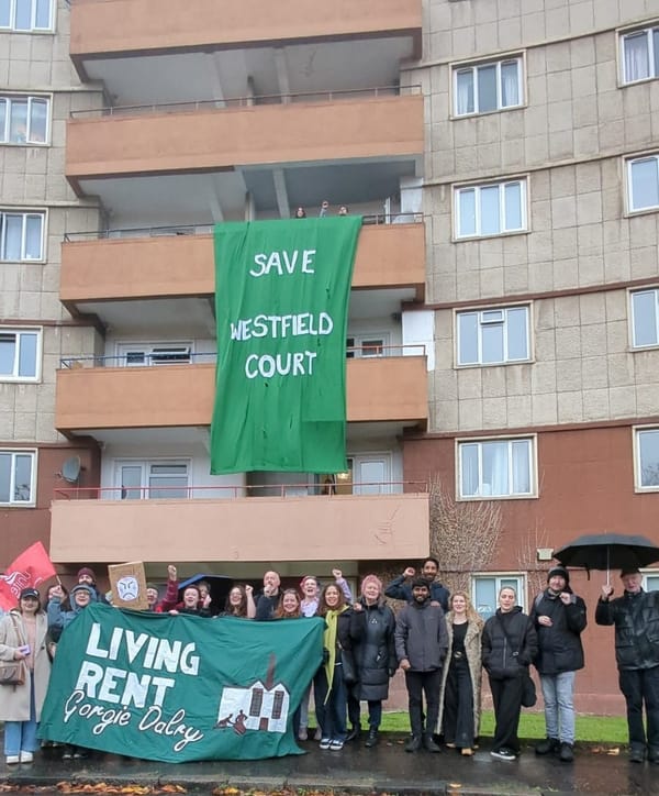 A group of people holding banners standing outside a block of flats. 