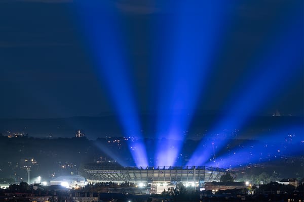 Purple and blue beams of light emanating from a stadium seen at night. 